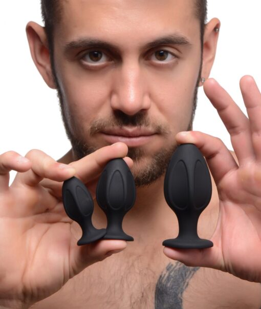 A man holding two black butt plugs in his hands.